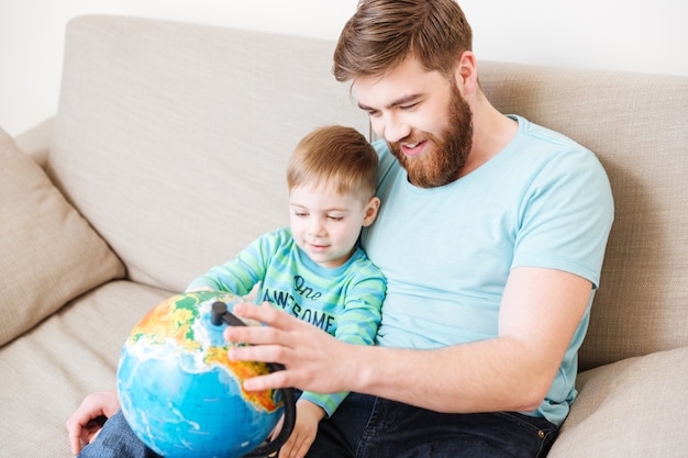 Foto feliz papá e hijo sentados y mirando el mundo juntos en casa