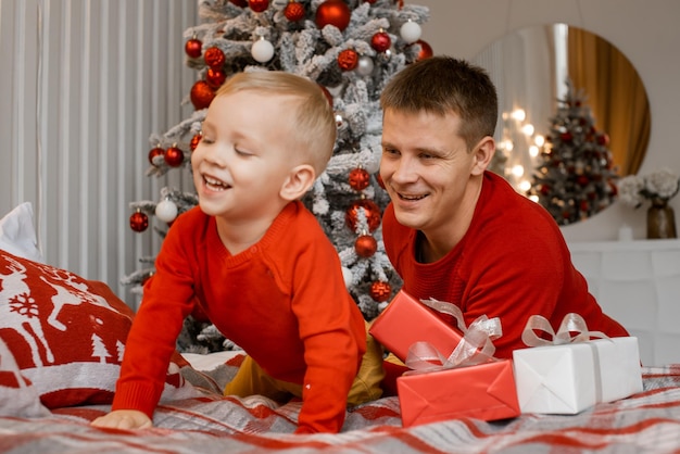 Feliz papá le hace cosquillas y se divierte con el pequeño hijo emocionado cerca del árbol de Navidad. Relájese juntos, padre cariñoso jugando con el niño sonriente. Concepto de vacaciones.