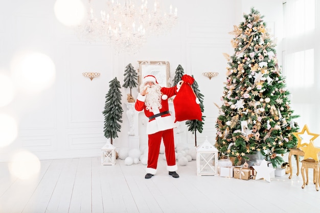 Feliz Papá Noel en el interior cerca del árbol de Navidad llevando regalos a los niños