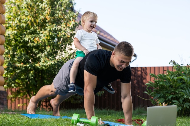 Feliz papai jovem está brincando com seu bebê em um gramado verde. conceito de uma família feliz. dia dos pais. pai e filho têm atividades juntos nos feriados no quintal