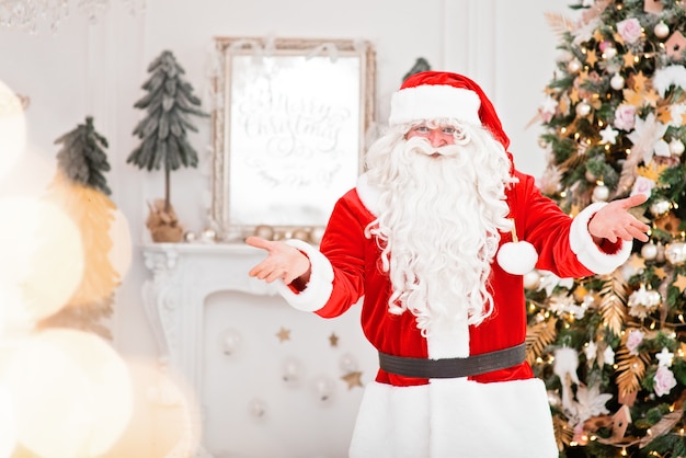 Feliz Papai Noel dentro de casa perto da árvore de Natal carregando presentes para as crianças