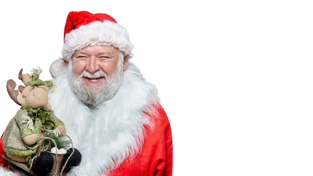 Feliz Papai Noel em um casaco vermelho, luvas e um chapéu, segurando um brinquedo nas mãos, apontando o dedo indicador, fundo branco isolado. Espaço para texto.