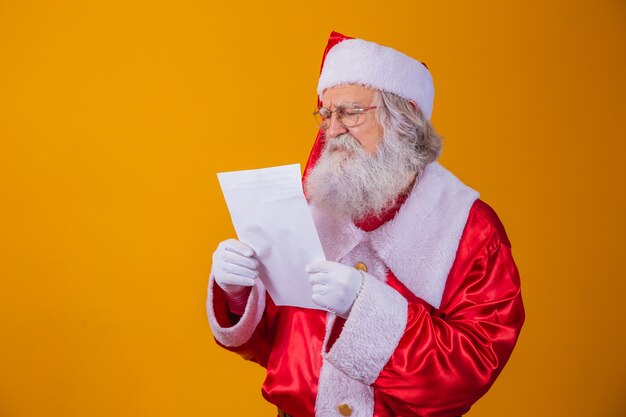 Feliz Papai Noel segurando papel vintage em fundo amarelo. Feliz Natal e conceito de véspera de ano novo. Copie o espaço. Dificuldade de leitura. Escrita feia.