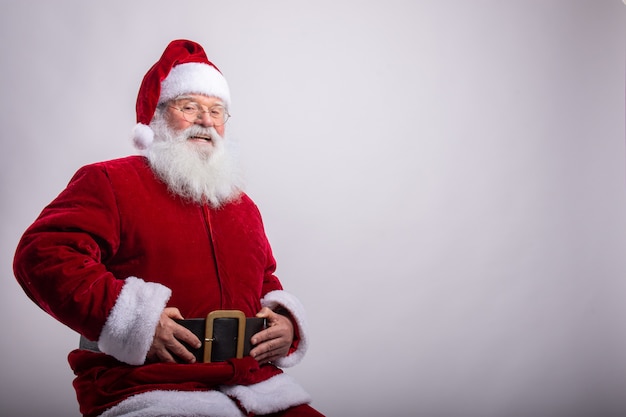 Feliz Papai Noel, sentado com as mãos no cinto na parede branca