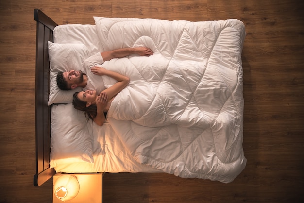 La feliz pareja se abraza en la cama. vista desde arriba