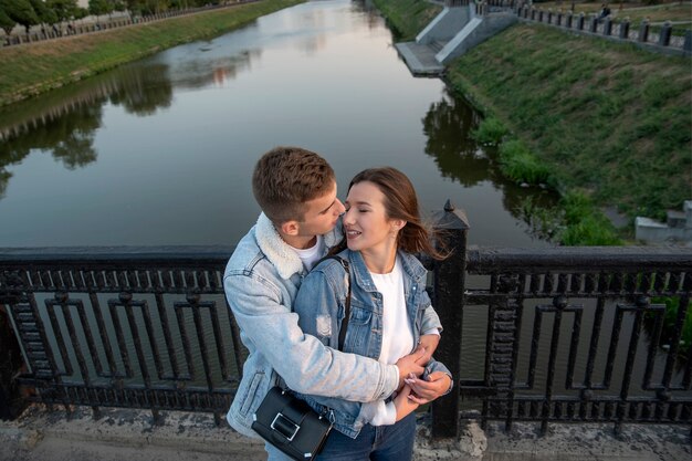 Feliz pareja abraza en el puente. Guy abraza y besa a su amada en el fondo del río. Vista anterior. Cita romántica.