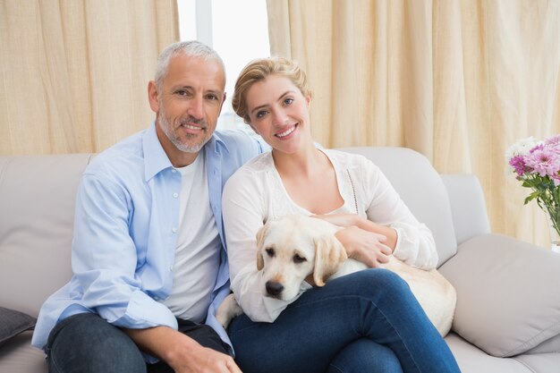 Feliz pareja abrazados con cachorro en el sofá