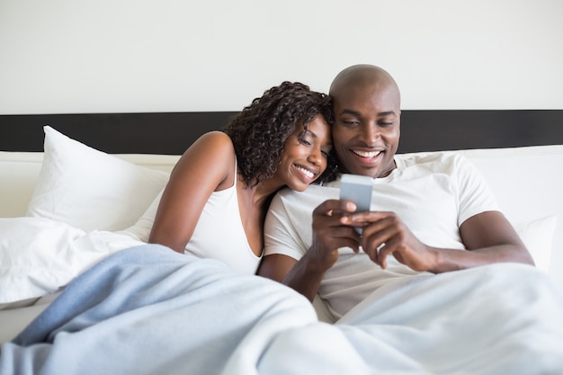 Feliz pareja abrazados en la cama con teléfono inteligente