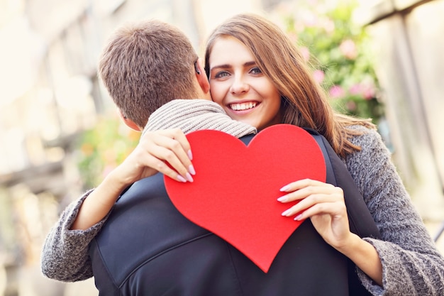 Foto feliz pareja abrazándose con flores y corazón en la ciudad