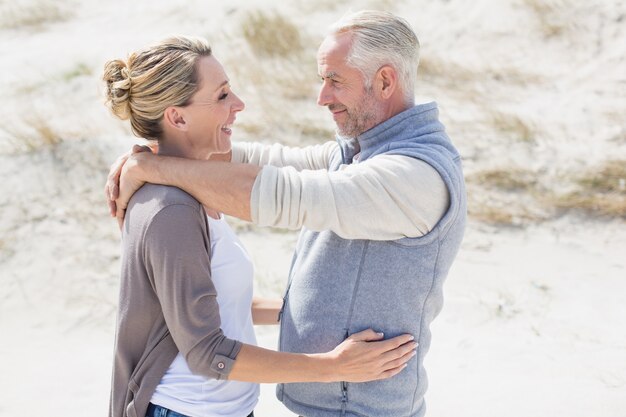 Feliz pareja abrazándose en la playa mirando el uno al otro