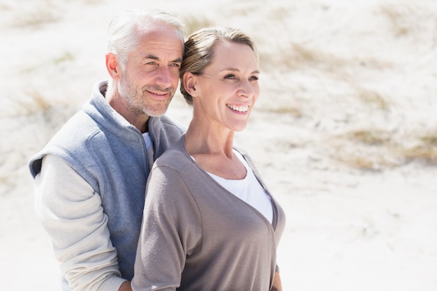 Feliz pareja abrazándose en la playa mirando a otro lado