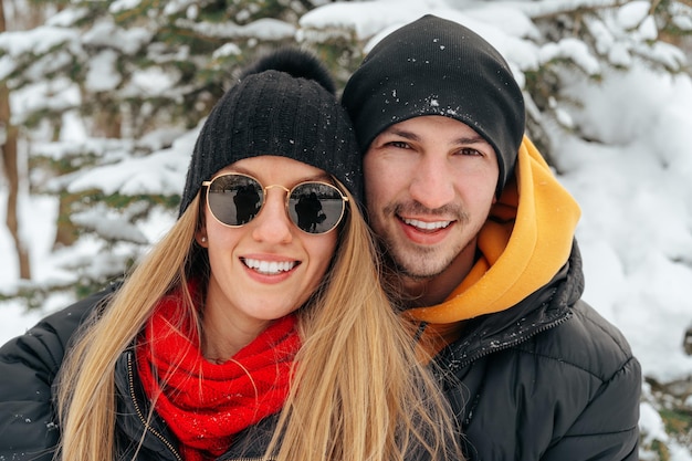Feliz pareja abrazándose y sonriendo al aire libre en el parque cubierto de nieve