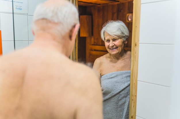 Feliz pareja de adultos mayores envueltos en toallas yendo a la sauna del spa