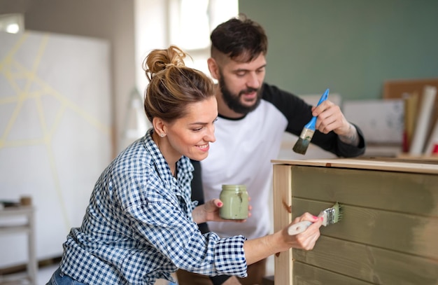 Feliz pareja de adultos mediados de pintar muebles en el interior de su casa, reubicación y concepto de bricolaje.