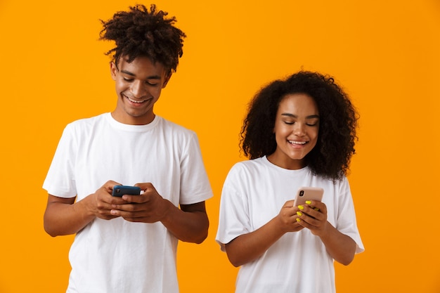 Feliz pareja africana linda joven aislada sobre el espacio amarillo mediante teléfonos móviles.
