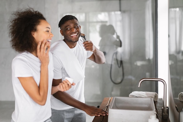 Una feliz pareja africana se preparan juntos cerca del espejo en el baño