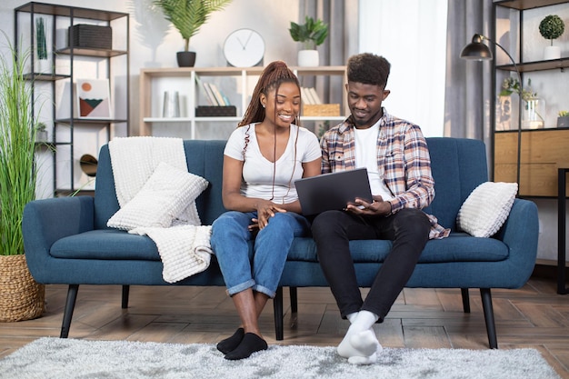 Feliz pareja africana usando una laptop en un cómodo sofá