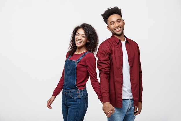 feliz pareja afroamericana cogidos de la mano y mirando hacia atrás aislado en blanco