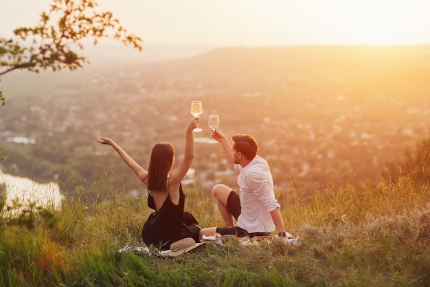 Feliz pareja alegre con las manos en alto disfrutar de la vista y la hermosa puesta de sol en un picnic de verano.