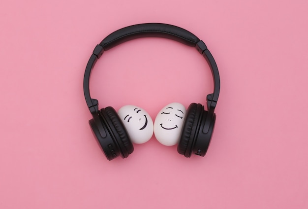 Feliz pareja amorosa de dos caras de huevo escuchar música en auriculares sobre fondo rosa