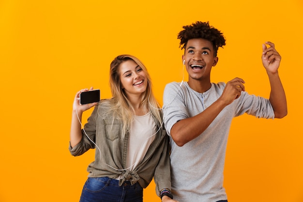 Feliz pareja amorosa joven bailando aislado sobre la pared amarilla escuchando música con auriculares