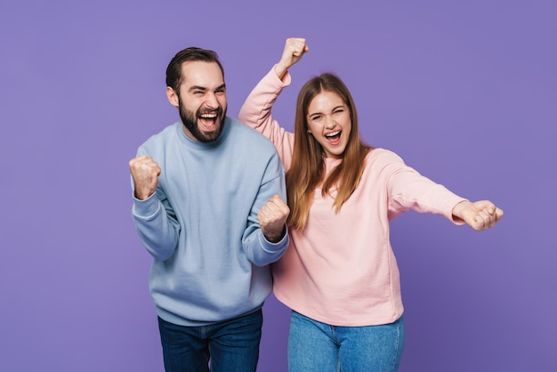 Feliz pareja amorosa optimista emocionado posando aislado sobre pared púrpura hacer gesto de ganador.