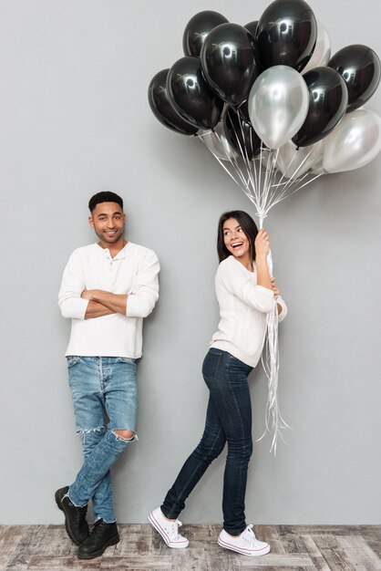 Feliz pareja amorosa de pie sobre la pared gris con globos