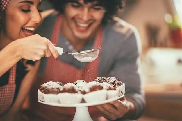 Foto una feliz pareja amorosa está rociando azúcar en polvo en un muffin de chocolate asado.