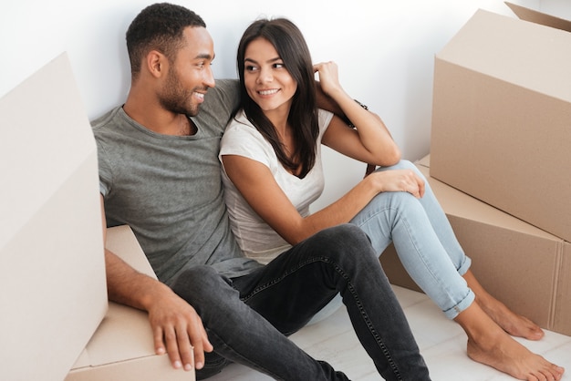 Feliz pareja amorosa tirada en el suelo con cajas desempaquetadas. Mirarse el uno al otro.