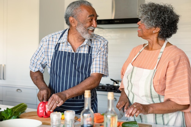 Feliz pareja de ancianos americanos africanos cortando verduras y preparando comida juntos