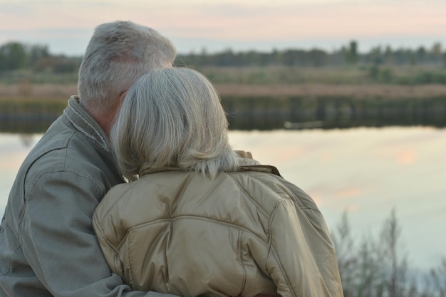 Una feliz pareja de ancianos cerca del lago durante la puesta de sol en verano