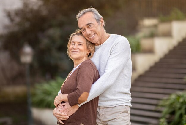 Feliz pareja de ancianos compartiendo un abrazo conmovedor de pie al aire libre en el parque