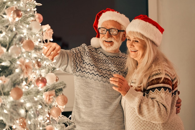 La feliz pareja de ancianos decorando el árbol de navidad