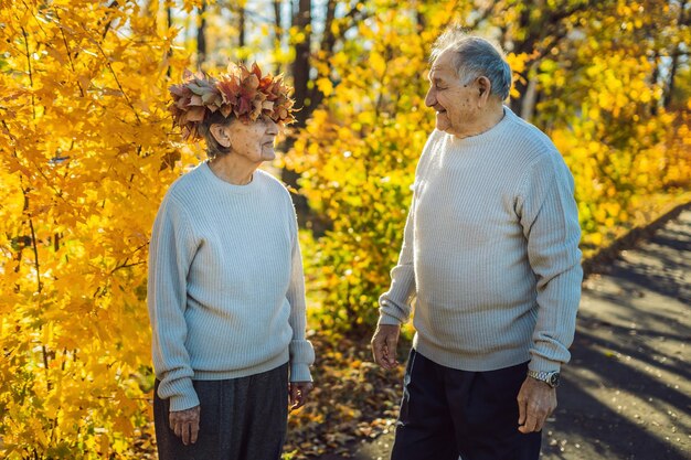 Feliz pareja de ancianos divirtiéndose en el parque de otoño. Anciano vistiendo una corona de hojas de otoño a su anciana esposa.