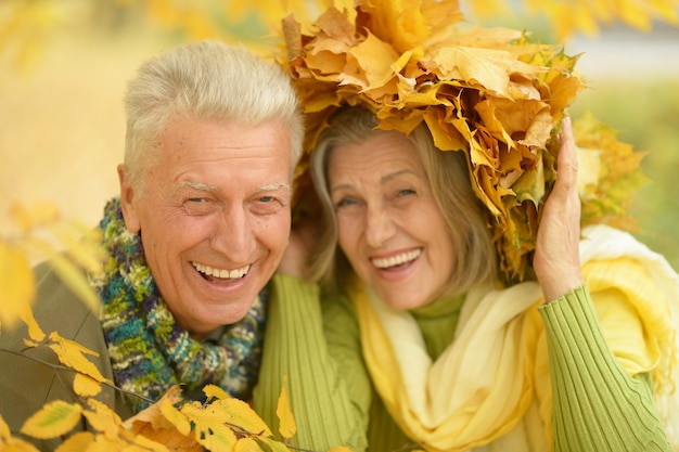 Feliz pareja de ancianos divirtiéndose en el parque de otoño, mujer en corona de hojas