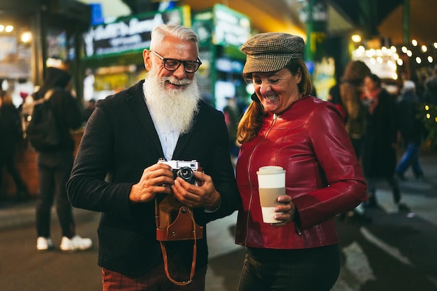 Feliz pareja de ancianos divirtiéndose tomando fotos con una cámara antigua en el mercado de comida callejera Enfoque en la cara del hombre