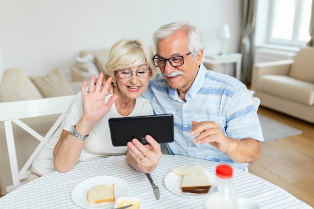 Feliz pareja de ancianos hablando con sus nietos usando tableta