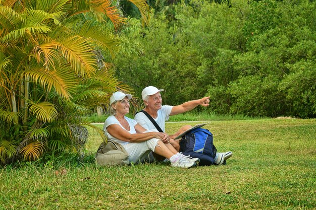 Feliz pareja de ancianos con mochilas en el jardín tropical al aire libre