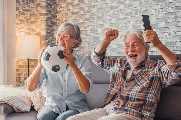 Feliz pareja de ancianos o fanáticos del fútbol viendo fútbol en la televisión y celebrando la victoria en casa Concepto de entretenimiento y deportes familiaresxA