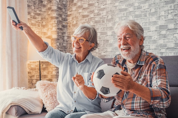 Feliz pareja de ancianos o fanáticos del fútbol viendo fútbol en la televisión y celebrando la victoria en casa Concepto de entretenimiento y deportes familiaresxA