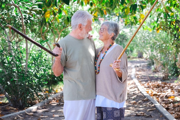 Feliz pareja de ancianos de pelo blanco caminando por el bosque con la ayuda de un bastón Sonrientes abuelos ancianos disfrutan de un estilo de vida saludable en un parque público