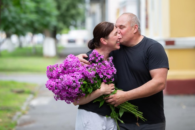 Una feliz pareja de ancianos con un ramo de flores camina por la ciudad de verano