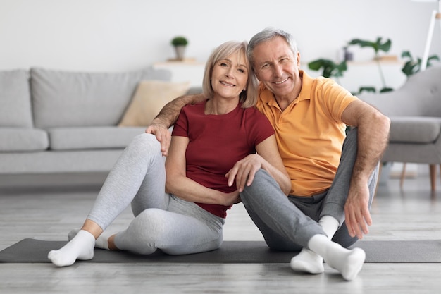 Feliz pareja de ancianos sentados en la alfombra de fitness en casa