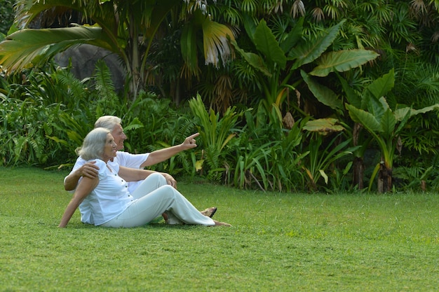 Feliz pareja de ancianos sentados en el césped en el jardín tropical al aire libre