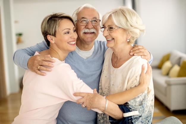 Feliz pareja de ancianos y su hija adulta abrazándose en casa