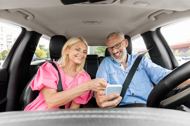 Feliz pareja de ancianos teniendo un viaje en coche juntos usando un teléfono celular