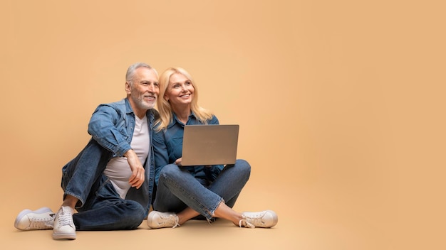 Feliz pareja de ancianos usando laptop mirando el espacio en blanco