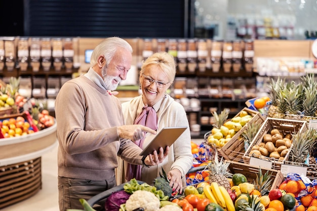 Una feliz pareja de ancianos usando una tableta para la lista de compras y comprando en el supermercado