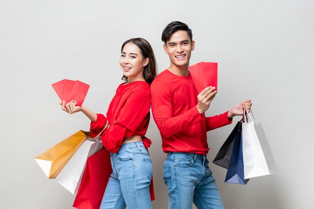 Feliz pareja asiática con bolsas de compras y sobres rojos aislados en un estudio gris para el concepto de venta de año nuevo chino