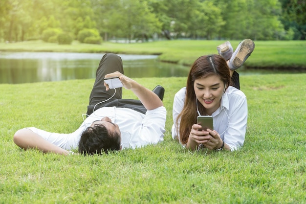 Feliz pareja asiática escuchando la canción a través de la cámara del teléfono inteligente en el parque
